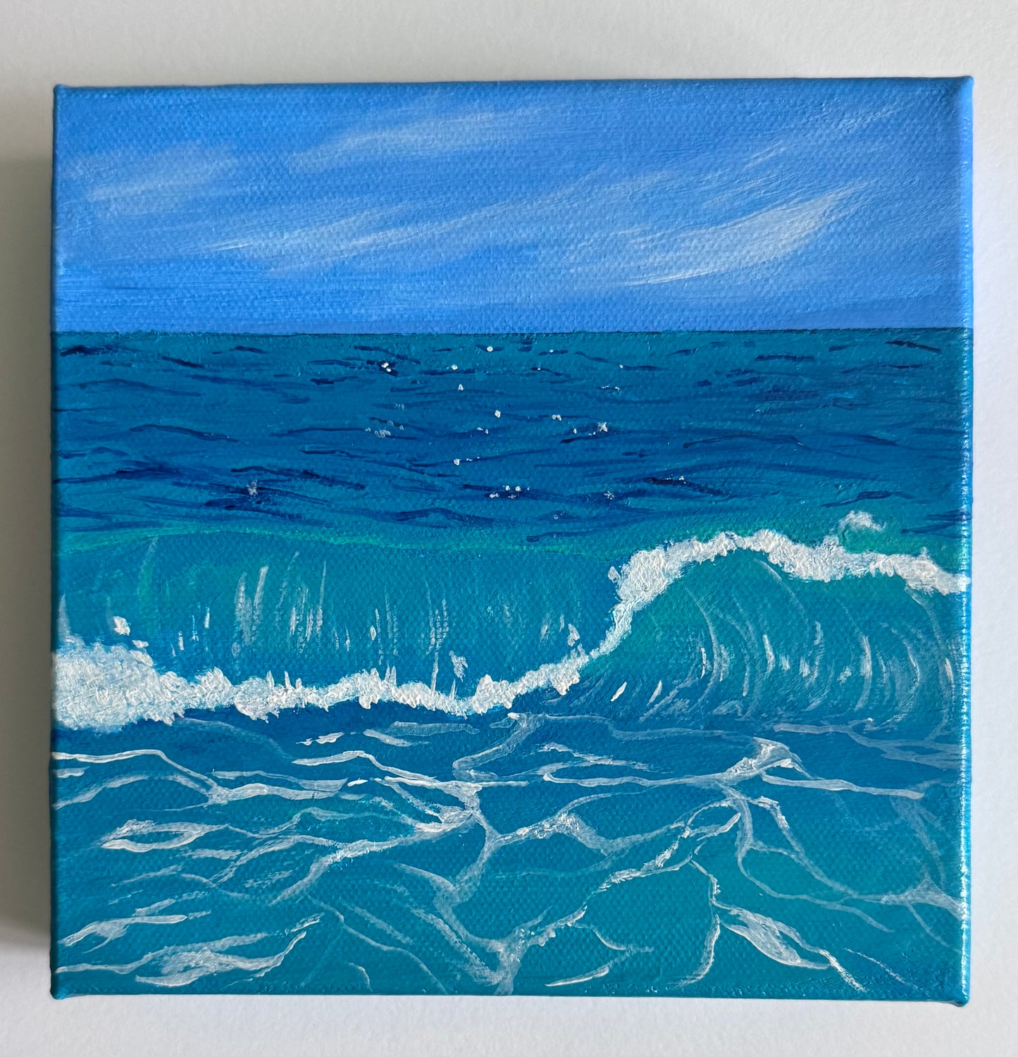 A square 6in x 6in canvas painting of a blue ocean with a breaking wave under a bright sky, shown against a plain light background