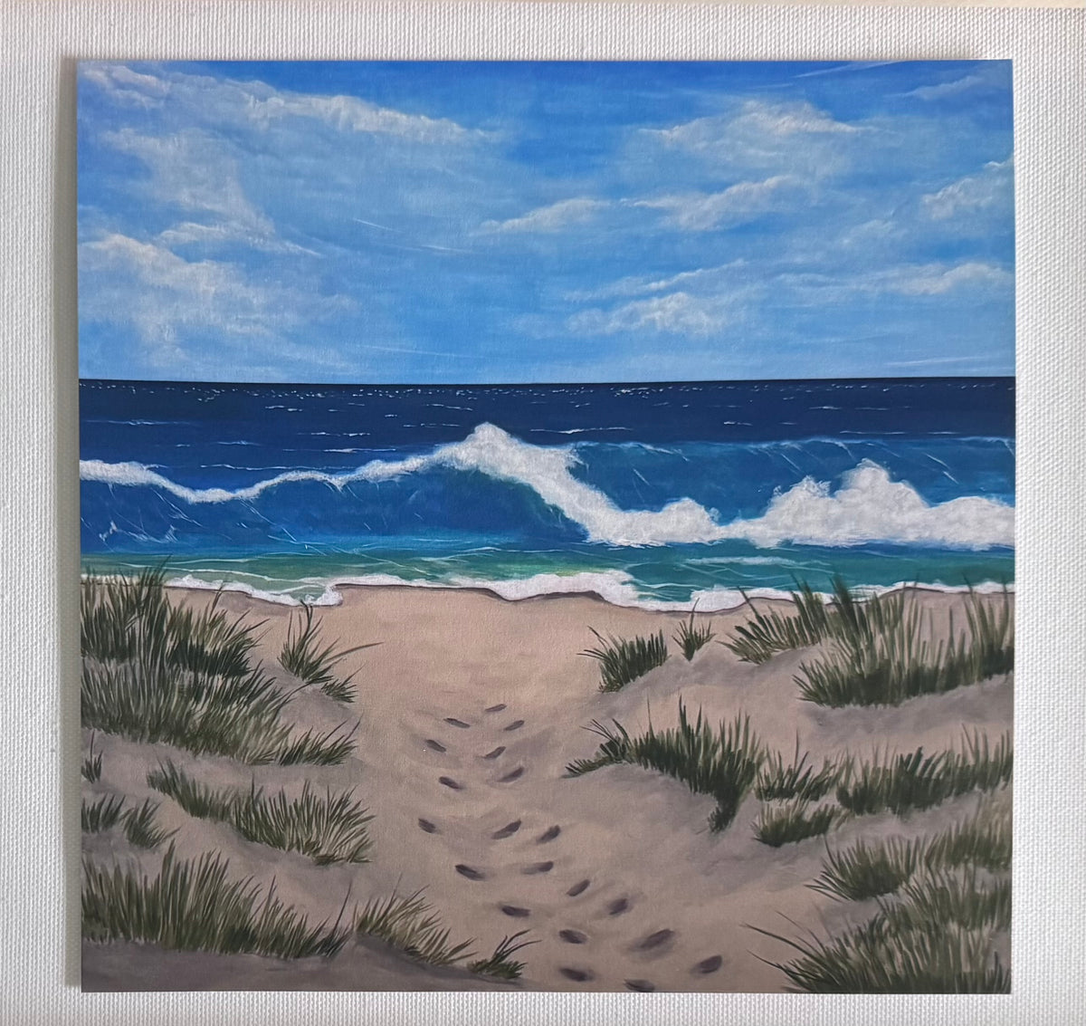 Art print without borders of a square painting of a beach scene with a sandy foreground, green dune grass, a blue ocean with white waves, and a bright blue sky with clouds